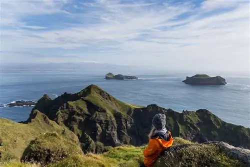Молодая женщина наблюдает за видом на океан на вершине Хеймаклеттура в Исландии