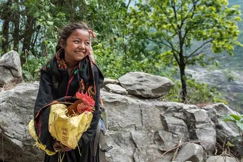 Молодая девушка со смехом несет своего петуха по тропе - регион Горха.
