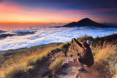 Фотограф снимает красивый восход солнца с помощью штатива, взятого с горы Батур, Бали, Индонезия.