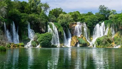 Маленькая лодка плывет прямо под водопадами Кравица на юге Боснии и Герцеговины.