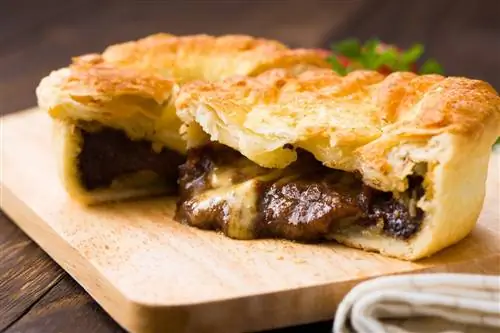 Слоеный, сочный мясной пирог на деревянной разделочной доске