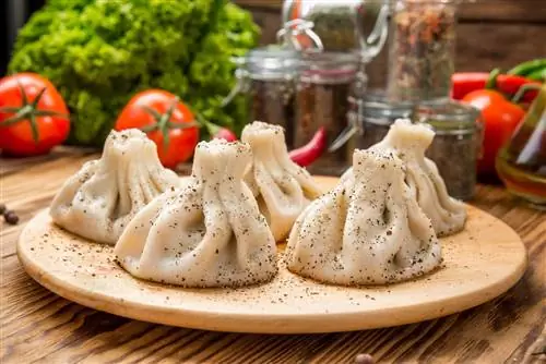 Грузинские пельмени хинкали с мясом, зеленью и томатным острым соусом сацебели на белой тарелке