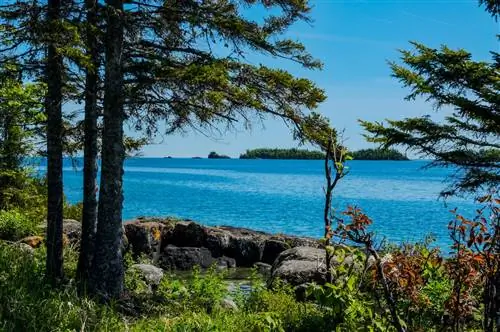 Вид через лес показывает несколько крошечных островов у главного острова Isle Royale NP в озере Верхнем у Коппер-Харбора, штат Мичиган. Большие валуны окружают небольшой бассейн с водой на берегу. Дайвинг на острове Рояль.