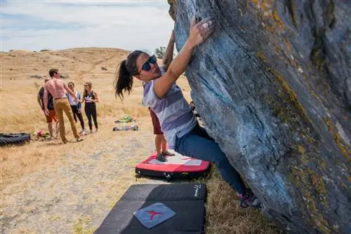 Молодая женщина взбирается на валун на Ринг-Маунтин, пока другие альпинисты разговаривают на заднем плане.