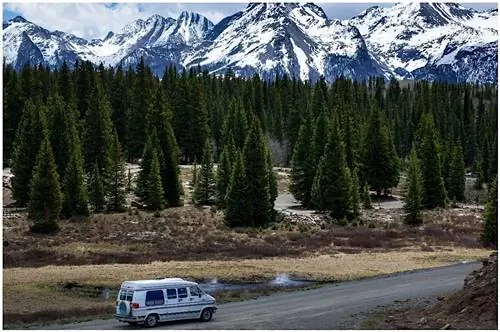 Фургон Van Life едет по дороге рядом с лесом и горами