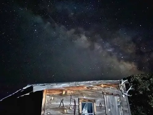 Темное небо со следом Млечного Пути за старым деревянным сараем