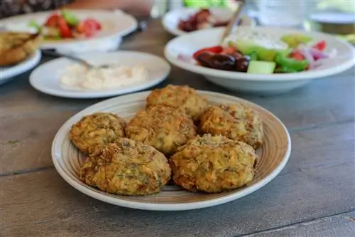 Тарелка с жареными кабачковыми шариками рядом с блюдом из греческого салата